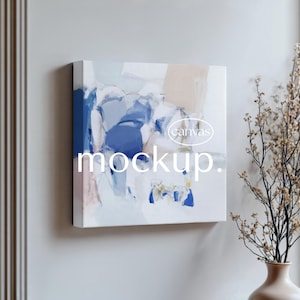 May include: Square canvas art with an abstract design in shades of blue, white, and beige. The word "mockup" is printed in white at the bottom of the canvas. The word "canvas" is printed in a white oval shape. The canvas is mounted on a light gray wall.