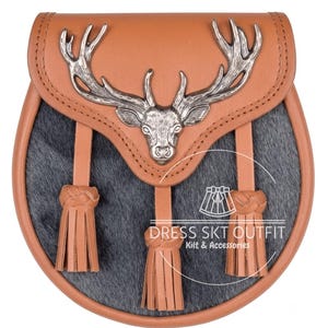 May include: A sporran featuring a tan leather flap with a silver-toned metal stag head emblem. The body is made of dark gray fur. Three tan leather tassels with braided tops hang from the flap. The text DRESS SKT OUTFIT Kilt & Accessories is visible.