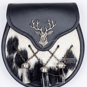 May include: A black and white cowhide sporran featuring a black leather flap with a silver-toned metal stag head emblem. The front includes three hanging tassels attached by silver-toned chains. The text DRESS SKT OUTFIT Kilt & Accessories is visible.