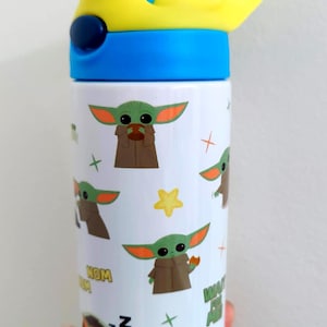 K&ouml;nnte beinhalten: Eine wei&szlig;e zylindrische Trinkflasche mit einem wiederkehrenden Muster aus einer gr&uuml;nen Alien-Figur mit gro&szlig;en Ohren, kleinen Fr&ouml;schen, gelben Sternen und dem Text "NOM NOM". Die Flasche hat einen blauen Deckel mit gelbem Klappverschluss.