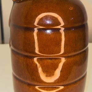 May include: A brown ceramic pitcher with a handle and a spout. The pitcher has a glossy finish and horizontal ridges around the body. The handle is rounded, and the spout is slightly curved.