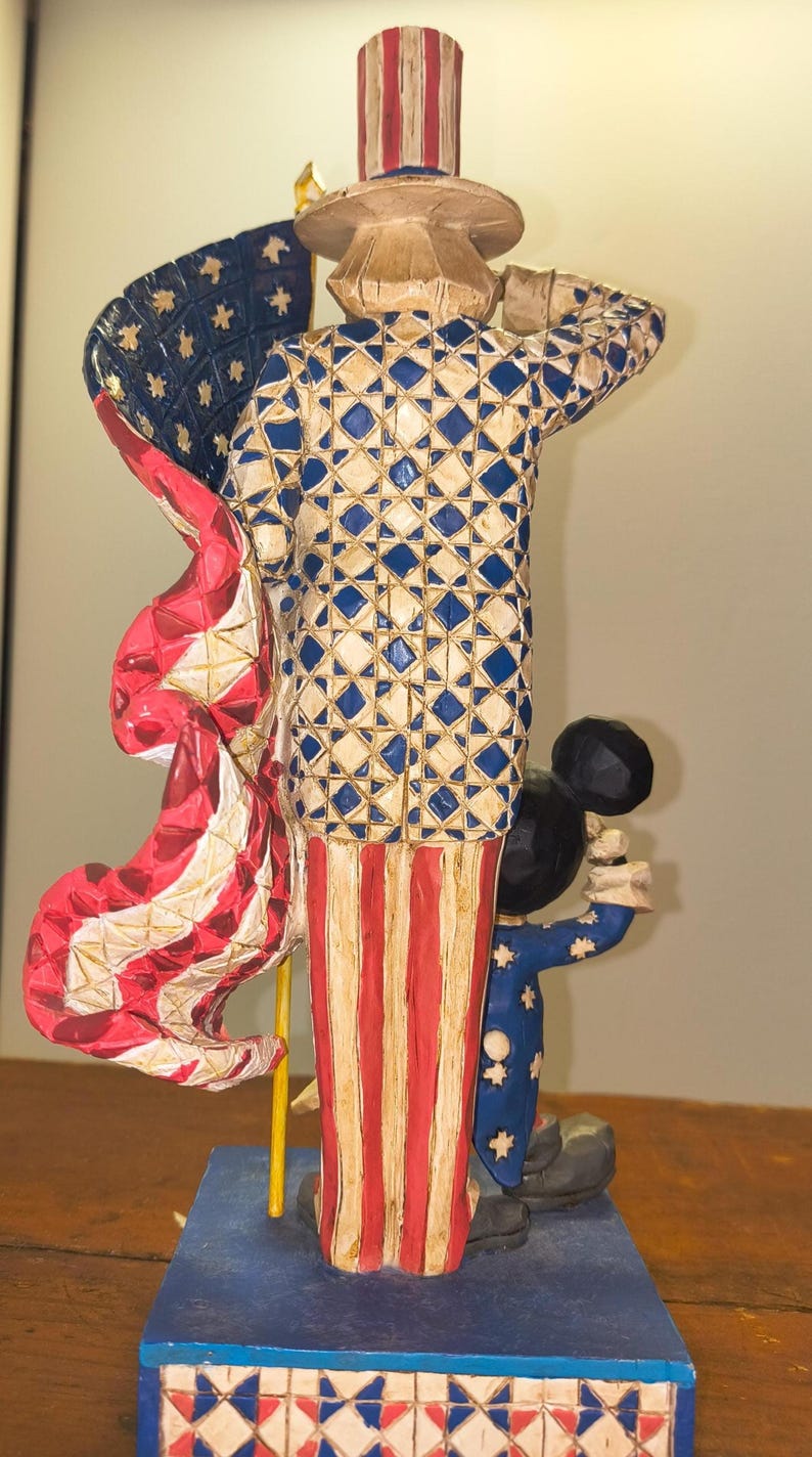 Puede incluir: Una figura patri&oacute;tica que presenta una figura con un atuendo y sombrero de copa con estrellas, sosteniendo una bandera. La figura es roja, blanca y azul. Tambi&eacute;n hay una figura m&aacute;s peque&ntilde;a con un atuendo azul con estrellas blancas. La base es azul con detalles en rojo y blanco.