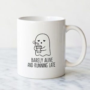 May include: A white ceramic mug with a black handle and the text "But First, Coffee" in a black, handwritten-style font. The mug is on a white surface.