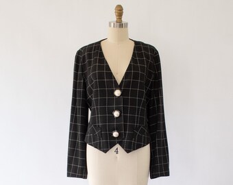 Könnte beinhalten: Ein schwarzer und weißer karierter, kurzer Blazer mit perlmuttartigen Knöpfen. Der Blazer befindet sich auf einer Schaufensterpuppe.