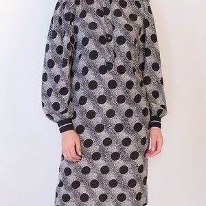 Peut inclure: Une robe &agrave; pois noirs et blancs avec un col blanc et des manches longues. La robe a un devant boutonn&eacute; et une silhouette ajust&eacute;e.