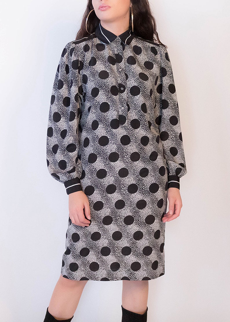 Peut inclure: Une robe &agrave; pois noirs et blancs avec un col blanc et des manches longues. La robe a un devant boutonn&eacute; et une silhouette ajust&eacute;e.