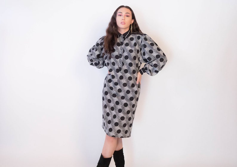 Peut inclure: Une robe &agrave; pois noirs et blancs avec un col blanc et des manches longues. La robe est mi-longue et cintr&eacute;e.
