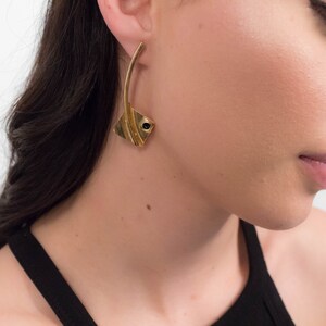 May include: A woman wearing a black tank top with gold earrings featuring a black stone accent.