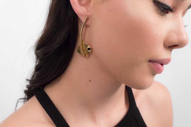 May include: A woman wearing a black tank top with gold earrings featuring a black stone accent.
