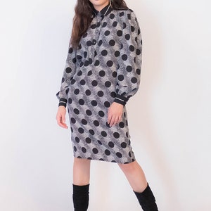 Peut inclure: Une robe &agrave; pois noirs et blancs avec un col et des manches longues. La robe a une silhouette ajust&eacute;e et arrive au niveau du genou. Le mannequin porte des bottes noires.