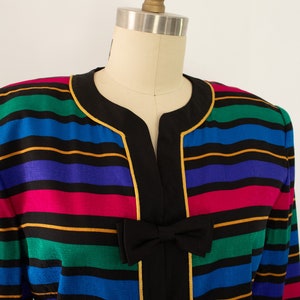 May include: A colorful striped blazer with a black collar and gold trim. The blazer has a V-neck and features a black bow at the front.