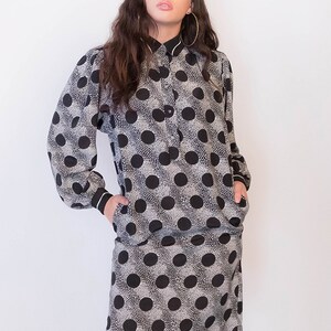 Peut inclure: Une robe &agrave; pois noirs et blancs &agrave; manches longues et col. La robe a une fermeture boutonn&eacute;e &agrave; l'avant et des poches sur les c&ocirc;t&eacute;s.