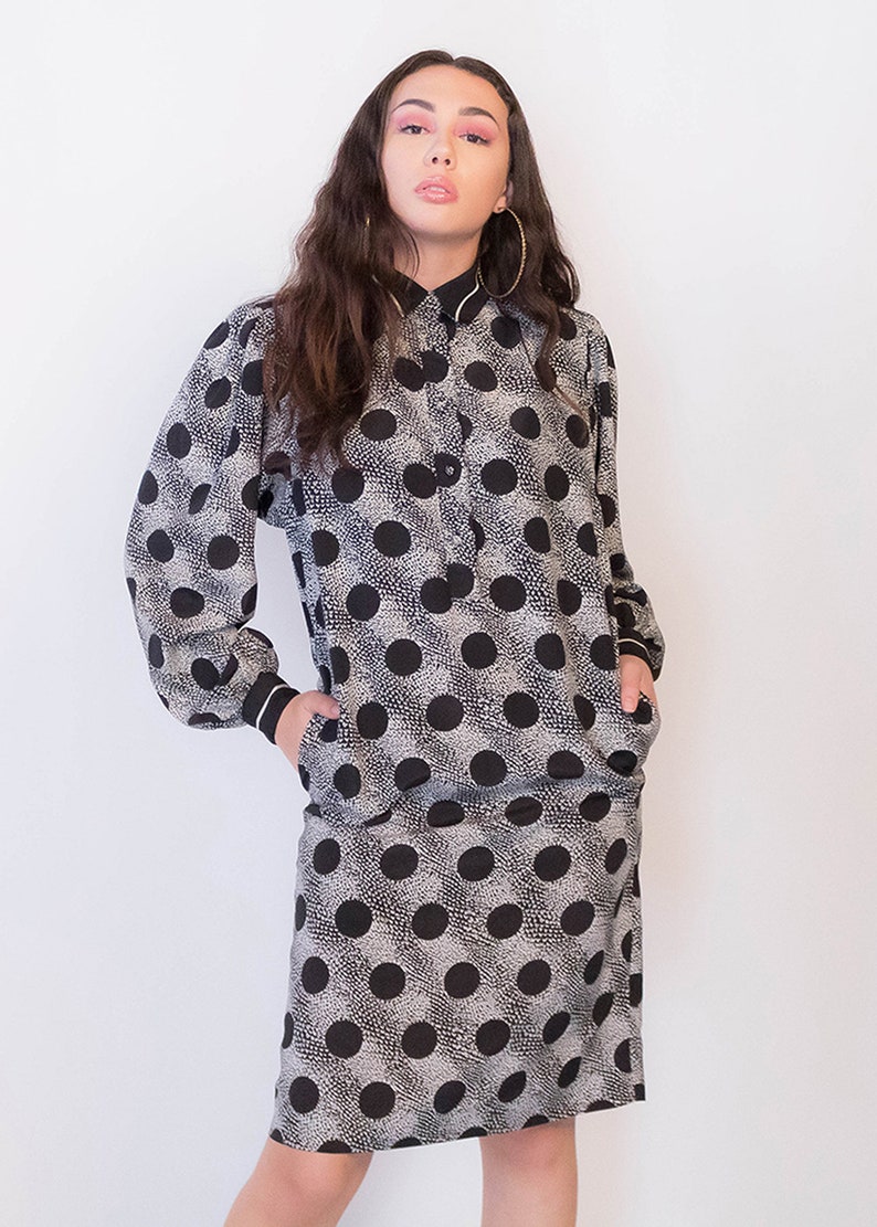 Peut inclure: Une robe &agrave; pois noirs et blancs &agrave; manches longues et col. La robe a une fermeture boutonn&eacute;e &agrave; l'avant et des poches sur les c&ocirc;t&eacute;s.