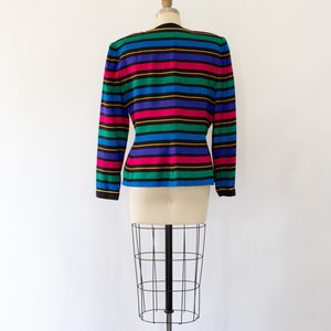 May include: A striped blazer with long sleeves in a variety of colors, including blue, green, pink, yellow, and black. The blazer is on a white mannequin.