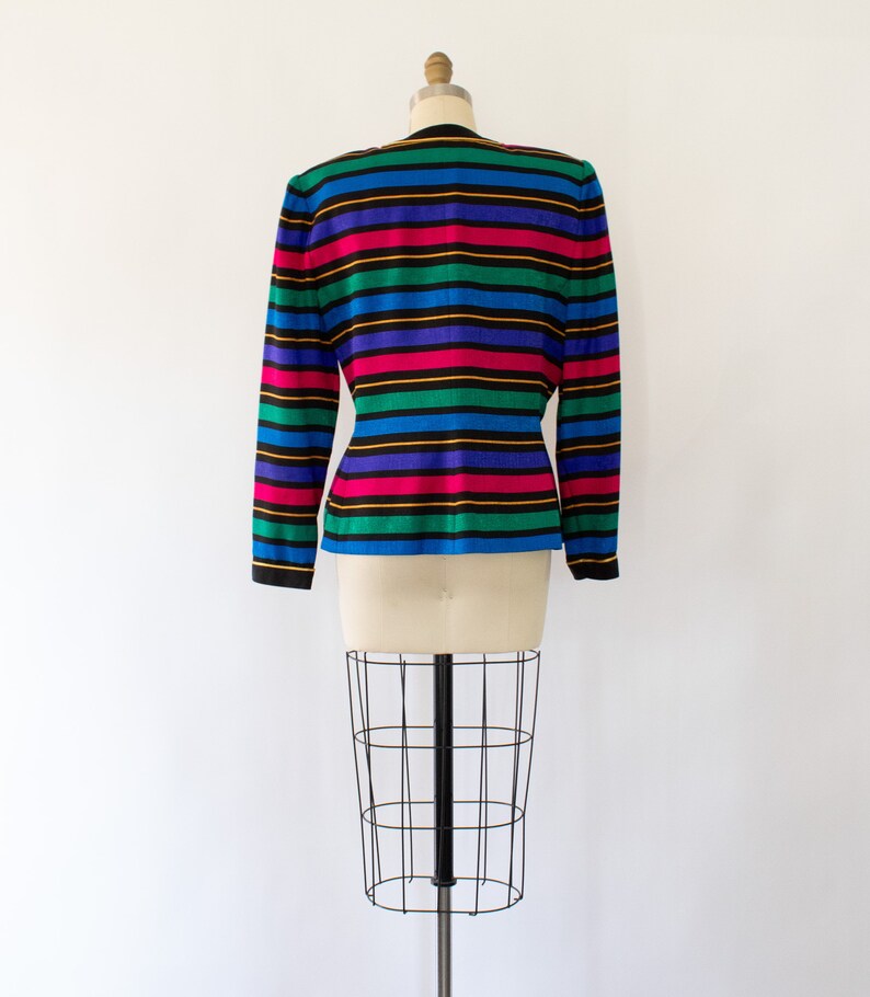 May include: A striped blazer with long sleeves in a variety of colors, including blue, green, pink, yellow, and black. The blazer is on a white mannequin.