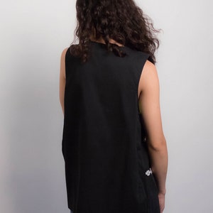 May include: A black sleeveless vest with a slightly longer back hem. The vest is made of a smooth, plain fabric.