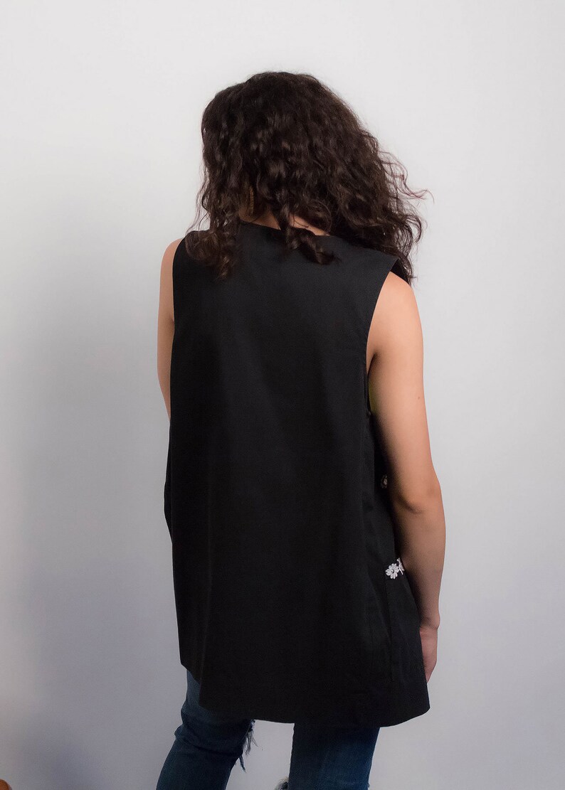 May include: A black sleeveless vest with a slightly longer back hem. The vest is made of a smooth, plain fabric.