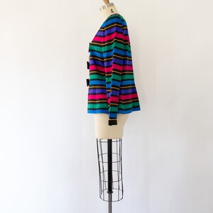 May include: A striped cardigan with a rainbow color scheme. The cardigan has black buttons and long sleeves.