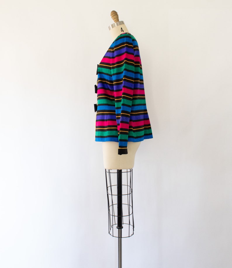 May include: A striped cardigan with a rainbow color scheme. The cardigan has black buttons and long sleeves.