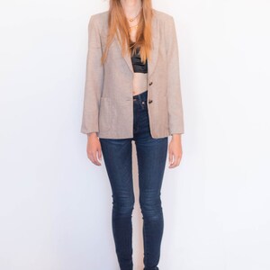 Puede incluir: Una mujer con un blazer marr&oacute;n claro sobre un sujetador negro y unos vaqueros azul oscuro. Lleva botines negros.