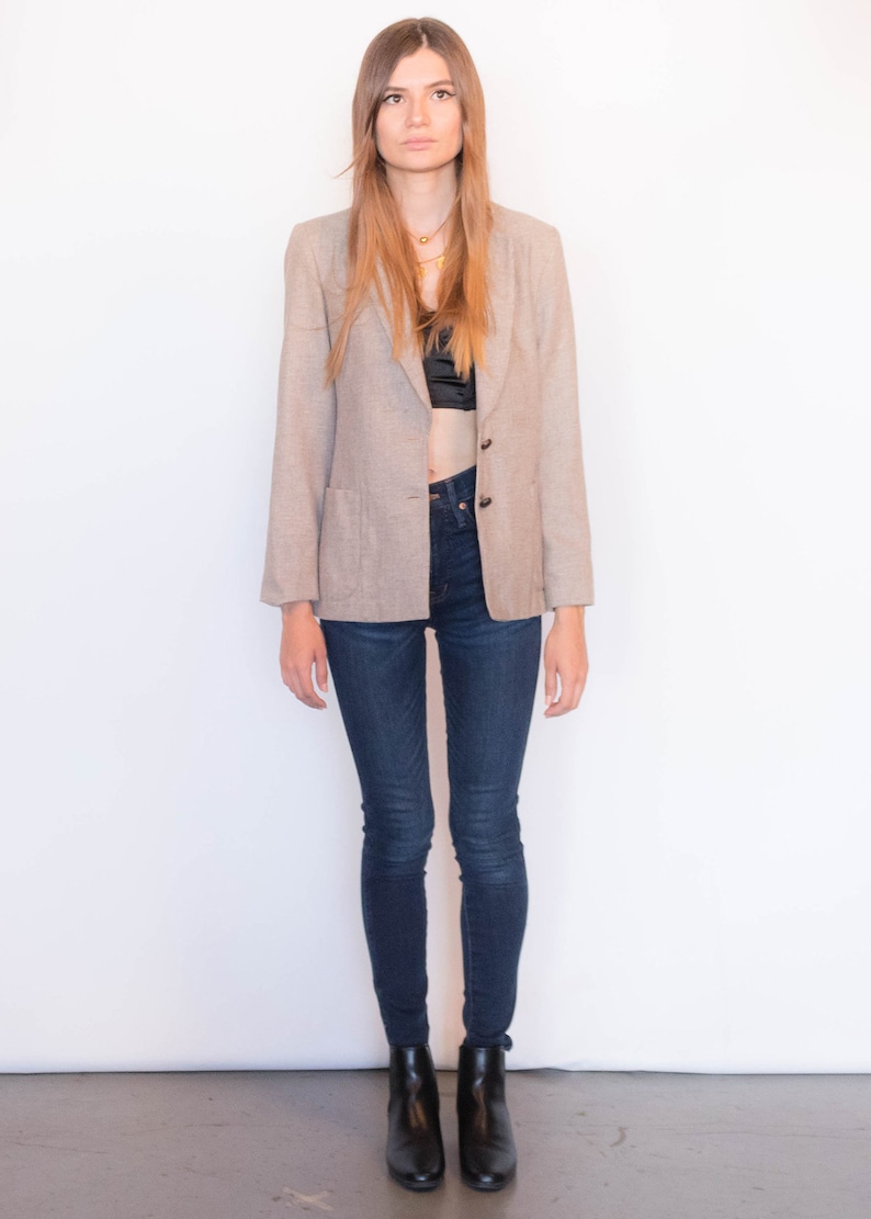 Puede incluir: Una mujer con un blazer marr&oacute;n claro sobre un sujetador negro y unos vaqueros azul oscuro. Lleva botines negros.