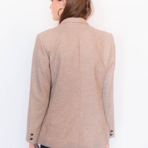 Puede incluir: Una chaqueta marr&oacute;n con un sutil estampado a cuadros. La chaqueta tiene cierre de doble botonadura y mangas largas con pu&ntilde;os abotonados.