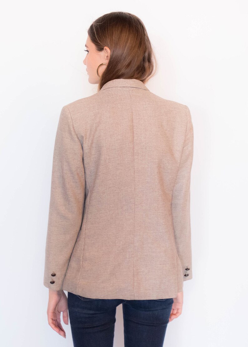 Puede incluir: Una chaqueta marr&oacute;n con un sutil estampado a cuadros. La chaqueta tiene cierre de doble botonadura y mangas largas con pu&ntilde;os abotonados.