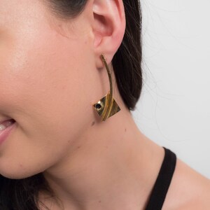 May include: Gold tone geometric earrings with a black stone accent. The earrings are long and dangle.