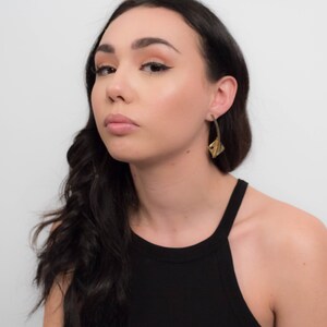 May include: A person with long dark hair wearing a black tank top and gold earrings. The earrings are shaped like a leaf.