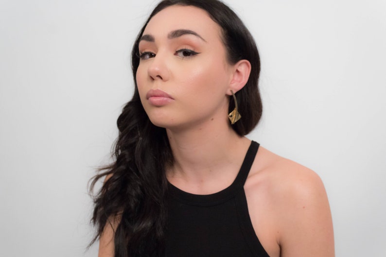 May include: A person with long dark hair wearing a black tank top and gold earrings. The earrings are shaped like a leaf.