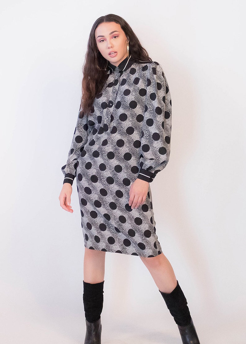 Peut inclure: Une robe &agrave; pois noirs et blancs avec un col et des poignets blancs. La robe a une silhouette ajust&eacute;e et des manches longues.