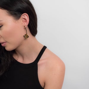 May include: A woman wearing a black tank top with gold geometric earrings. The earrings are long and dangle from the earlobe.