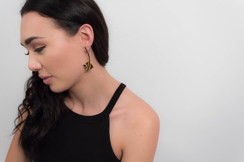 May include: A woman wearing a black tank top with gold geometric earrings. The earrings are long and dangle from the earlobe.
