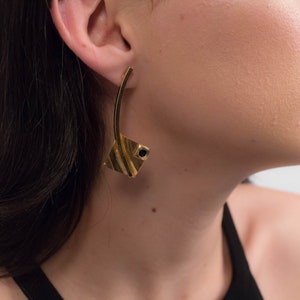 May include: A pair of gold earrings with a geometric design. The earrings have a black stone in the center of the geometric design.