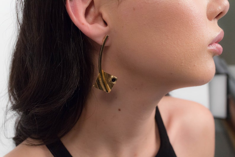 May include: A pair of gold earrings with a geometric design. The earrings have a black stone in the center of the geometric design.