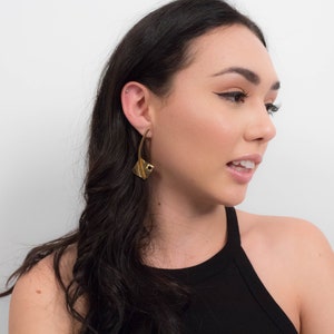 May include: A woman with long dark hair wearing a black tank top and gold geometric earrings.