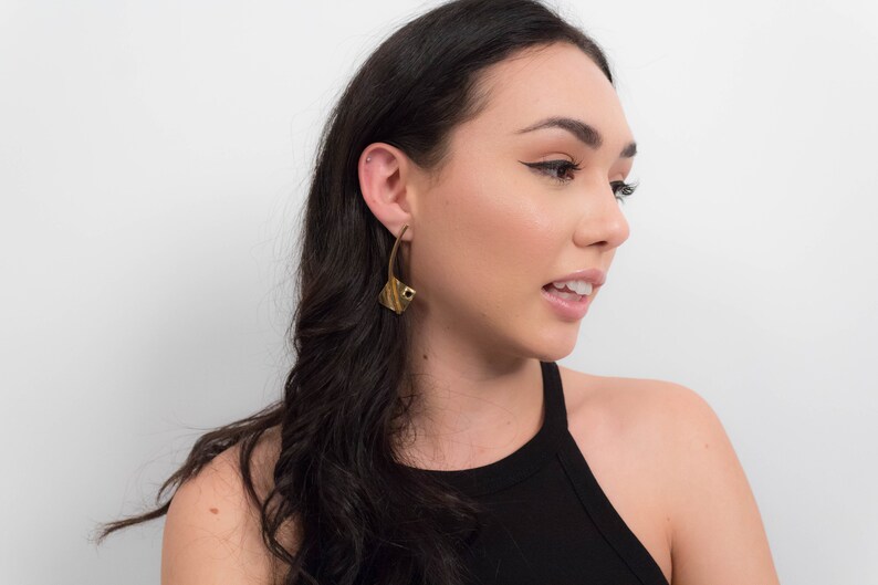 May include: A woman with long dark hair wearing a black tank top and gold geometric earrings.