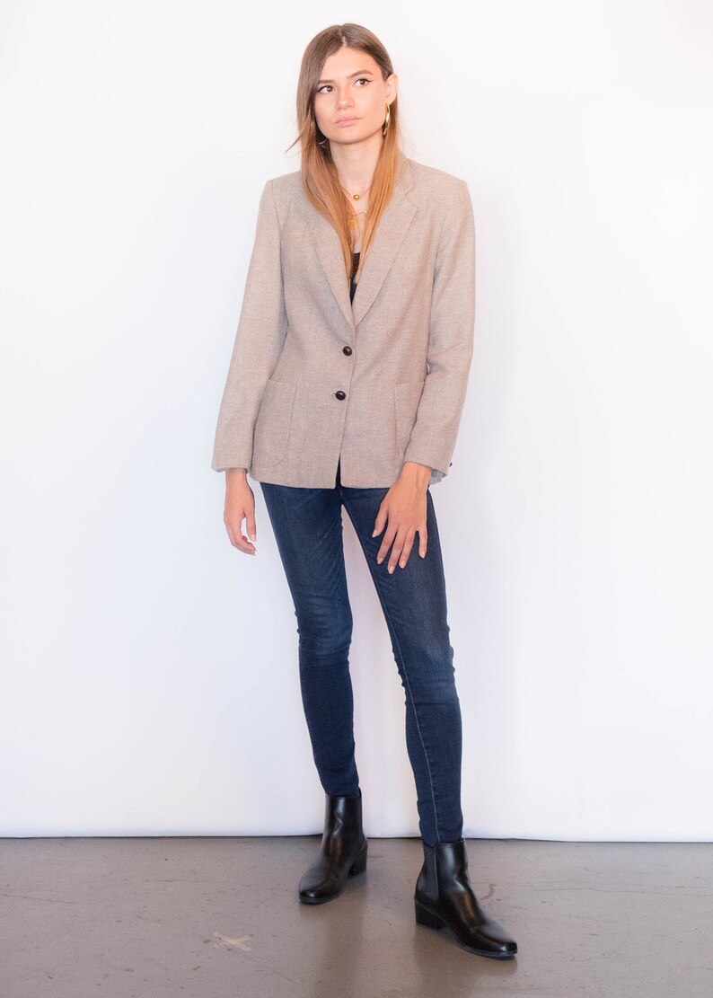 Puede incluir: Una mujer con un blazer marr&oacute;n claro con cierre de bot&oacute;n, jeans azul oscuro y botines negros.