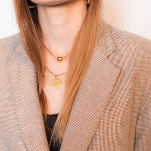 Puede incluir: Una mujer con un blazer marr&oacute;n, un collar de cadena dorada y pendientes de aro dorados.