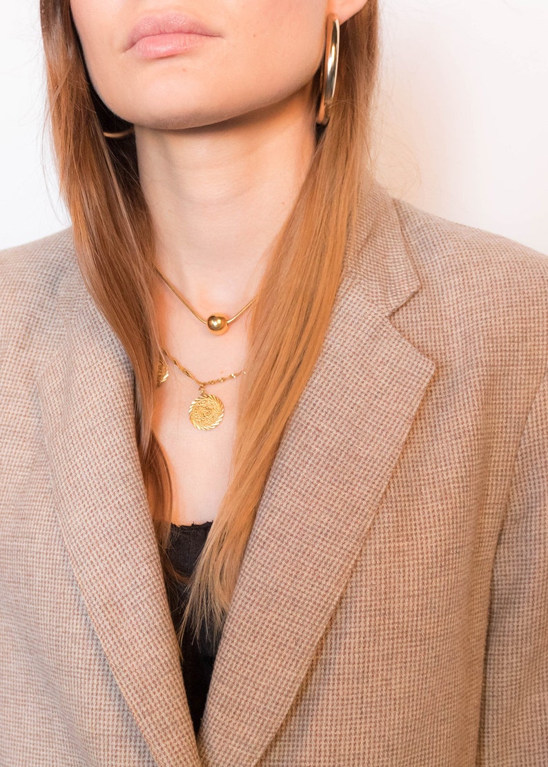 Puede incluir: Una mujer con un blazer marr&oacute;n, un collar de cadena dorada y pendientes de aro dorados.