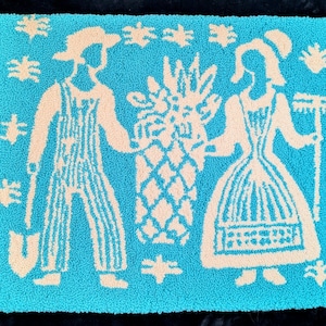 Könnte beinhalten: Türkisfarbener Teppich mit cremefarbenem Design, das einen Mann in Latzhosen mit einer Schaufel und eine Frau mit einer Harke zeigt, beidseitig einer Ananas. Der Teppich hat einen geschlungenen Flor und sternförmige Akzente.