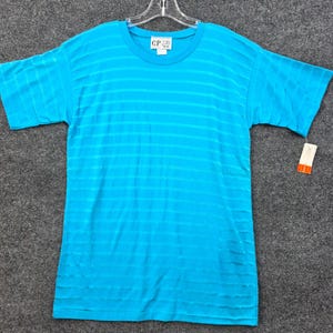 May include: A bright turquoise short-sleeve t-shirt featuring a subtle horizontal striped pattern throughout the fabric. The shirt has a round neckline and a white brand label at the inner collar that reads C.P. with a small tag attached to the side.