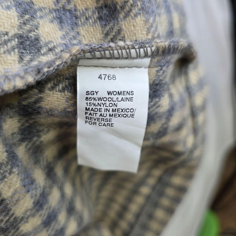 May include: A garment tag with the text 4768, SGY, 85% WOOL/LAINE, 15% NYLON, MADE IN MEXICO/FAIT AU MEXIQUE, and REVERSE FOR CARE, attached to a textured fabric featuring a blue and cream houndstooth pattern with a soft, fuzzy appearance.