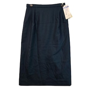 May include: A dark teal pencil skirt with a straight silhouette. The skirt has a high waist with two decorative metal clasps and a small tag attached. The fabric appears to be a woven material.