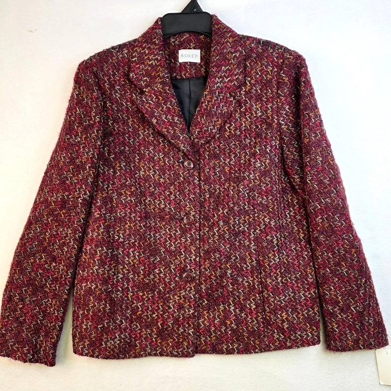 May include: A burgundy blazer with a textured weave pattern. The blazer has a notched collar, a single-button closure, and long sleeves. The lining is black, and the brand name "KOREN" is visible on a label.