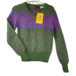 May include: A vintage V-neck sweater with a colorful pattern. The sweater features a green base with a repeating pattern of pink dots, a purple band with a red design, and green sleeves and cuffs. A yellow Levi's tag hangs from the neckline.