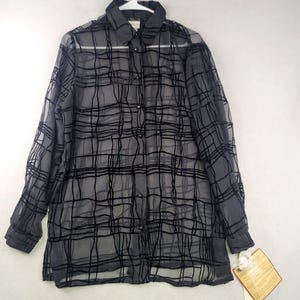 May include: A sheer black button-down shirt with a grid pattern. The long-sleeved blouse has a collared neckline and buttons down the front. A tag hangs from the bottom of the shirt. The shirt is hanging on a white hanger.
