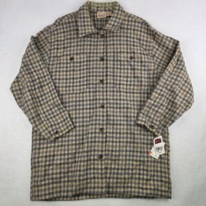May include: A long-sleeve button-down shirt featuring a tan and dark gray plaid pattern. The shirt includes a pointed collar, two chest pockets with button closures, and buttoned cuffs. A Woolrich brand tag is visible at the neck and on a hang tag.