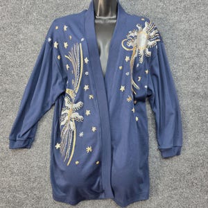 May include: A navy blue open-front cardigan featuring long sleeves and an embroidered celestial design. The embroidery includes silver and gold sun motifs, shooting stars, and various small star shapes scattered across the front panels.