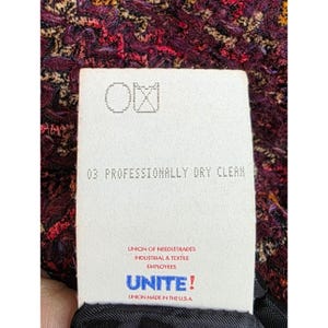 May include: Close-up of a tag with the text "03 PROFESSIONALLY DRY CLEAN" and the logo of the Union of Needletrades, Industrial & Textile Employees. The tag is against a textured, multi-colored fabric.